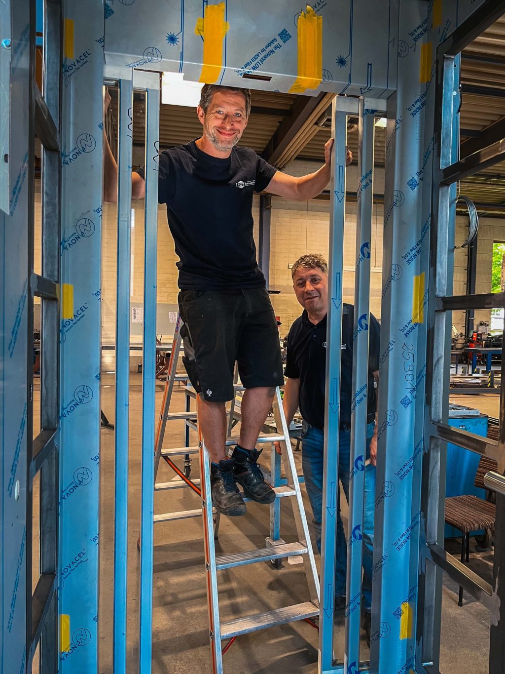 Orba Mitarbeiter lächeln in die Kamera und arbeiten am Aufzugsgerüst