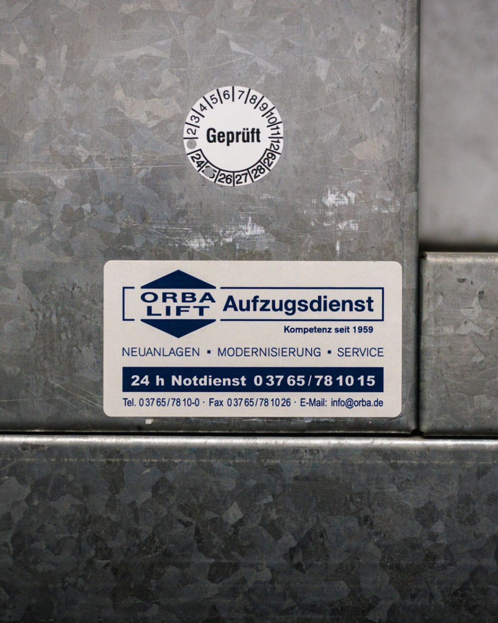 ORBA-Lift Logo mit Notrufnummer an der Außenseite eines Kleingüteraufzugs