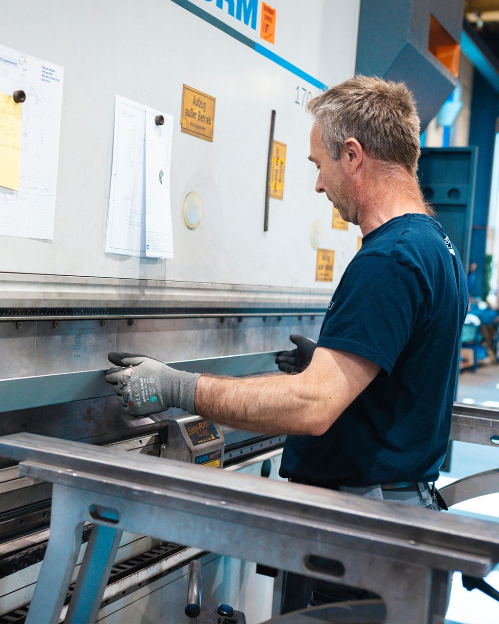 Nahaufnahme eines Arbeiters im Profil, der ein Metallblech präzise in eine LVD Abkantpresse einlegt.