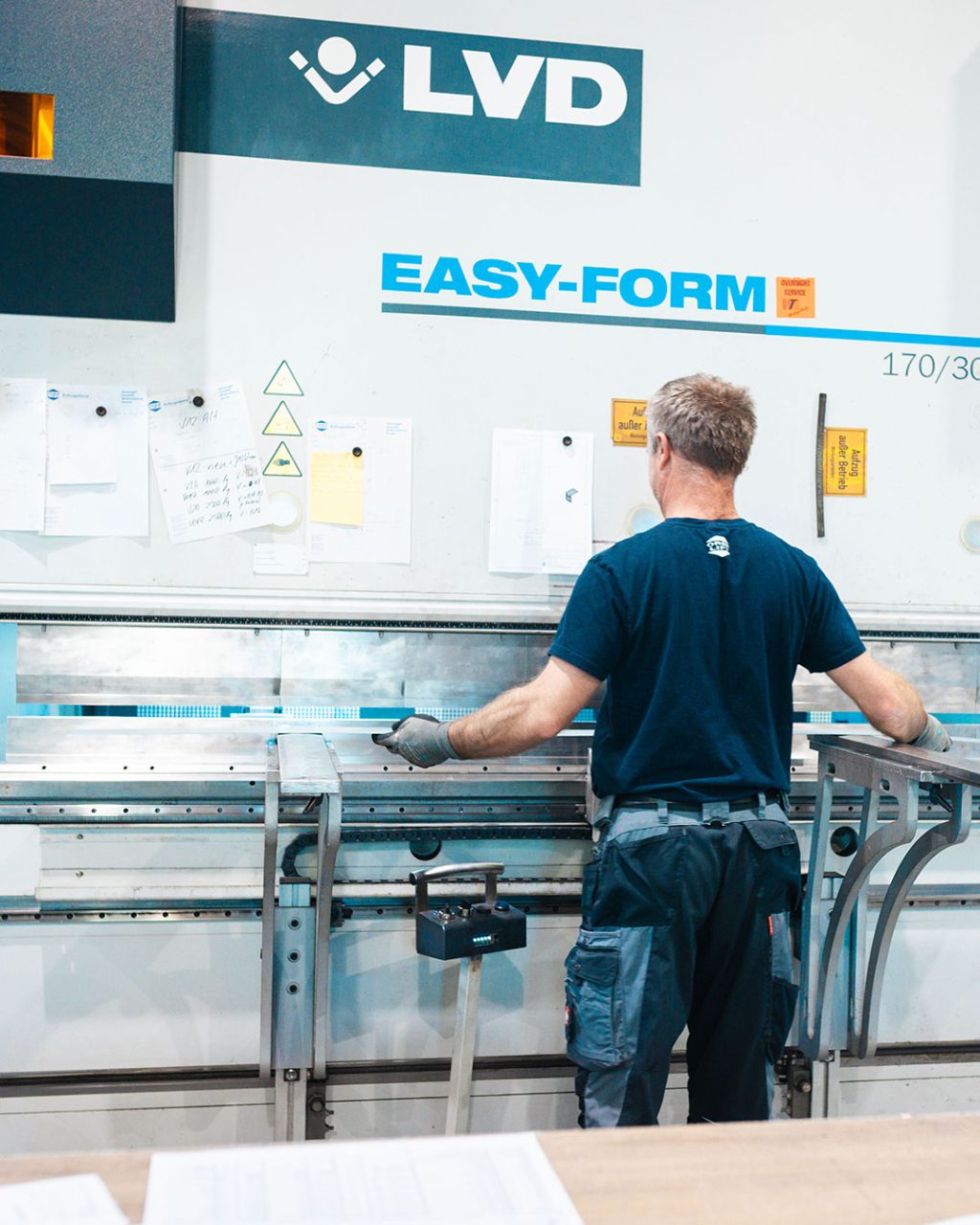 Ein Arbeiter von hinten bedient eine LVD Easy-Form Abkantpresse in einer Industriehalle.