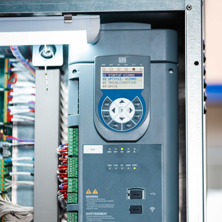 Nahaufnahme eines grauen WEG ADL550 Frequenzumrichters in einem Schaltkasten mit beleuchtetem Display, Bedienelementen und farbigen Verkabelungen.