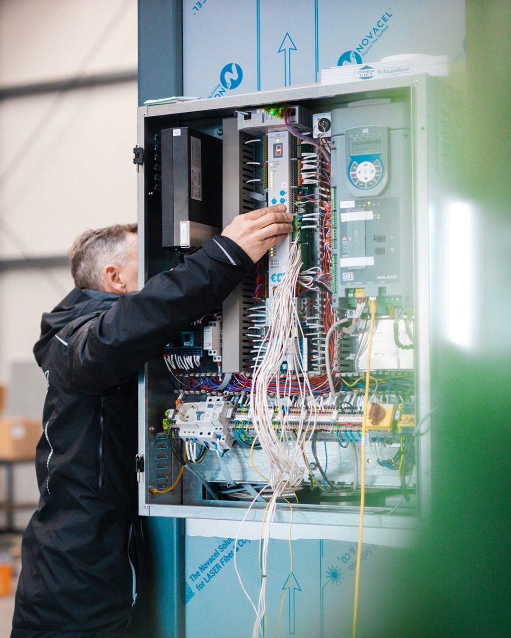Techniker im schwarzen Arbeitshemd arbeitet an den Modulen und der Verkabelung eines geöffneten Schaltschrankes.