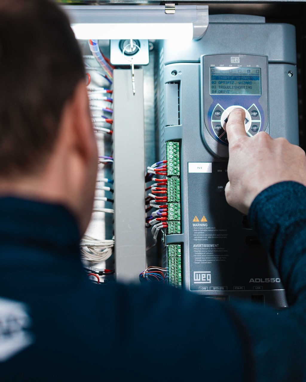 Nahaufnahme eines Techniker-Fingers, der eine Taste auf dem Bedienfeld eines WEG ADL550 Frequenzumrichters drückt.